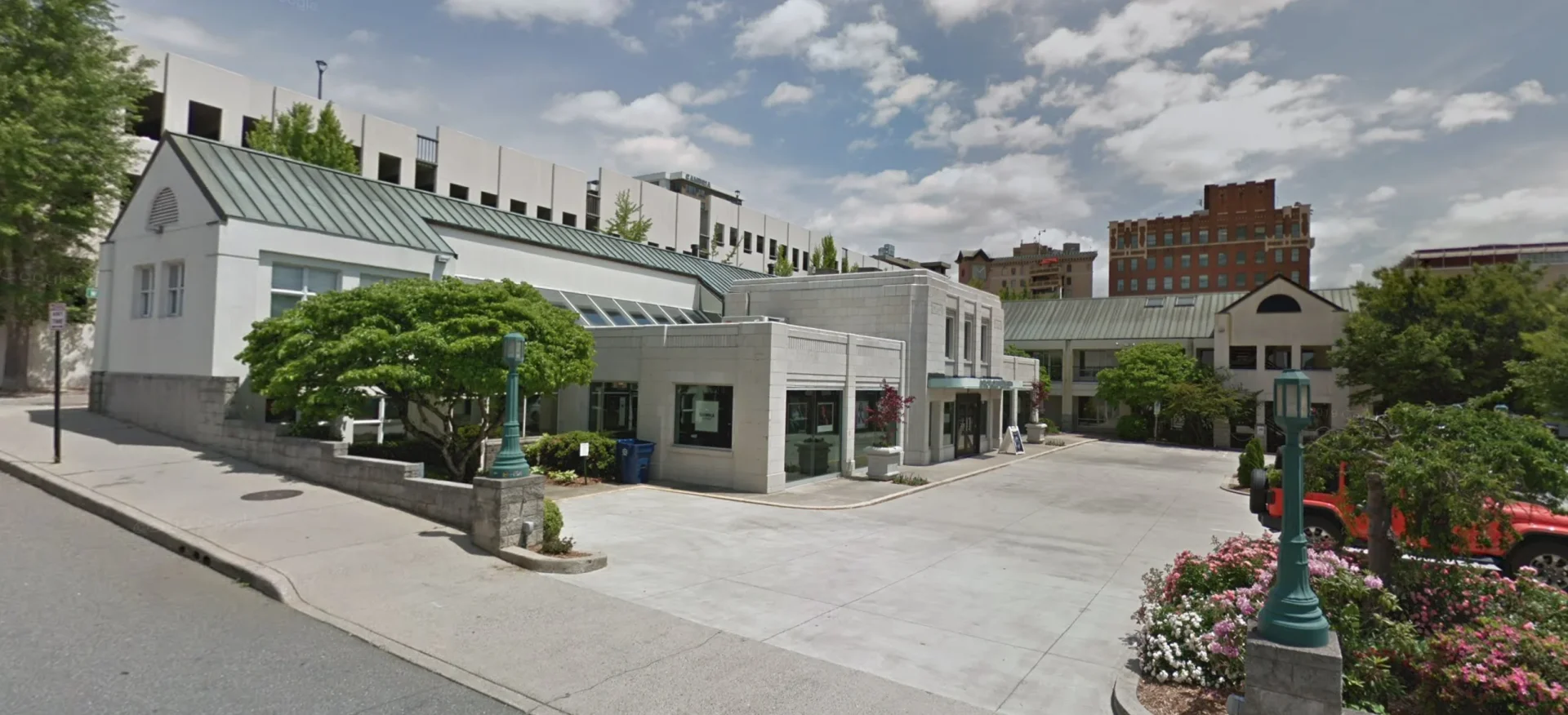 Photo of a architecturally interesting building against a blue cloudy sky and large social space in front covered with pavers.