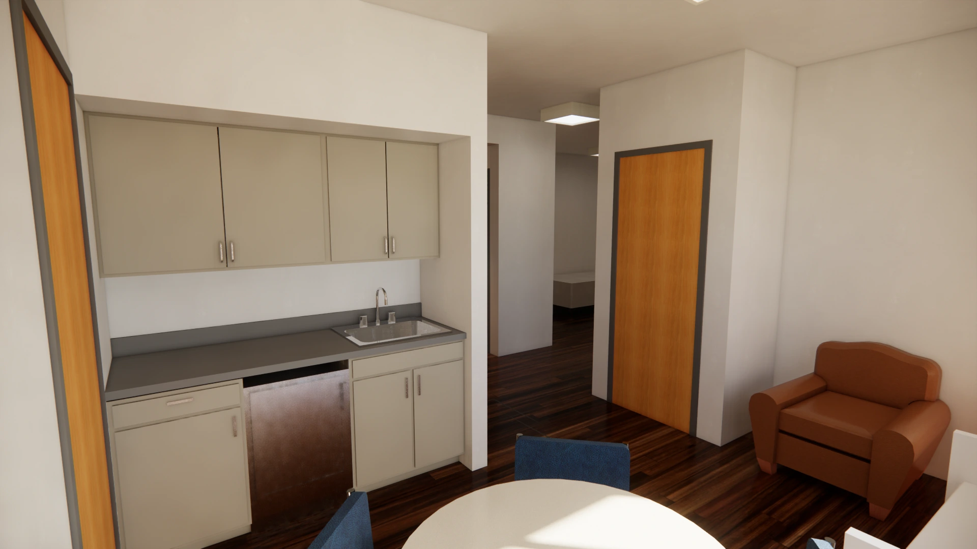A small kitchen area with beige cabinets and a stainless steel sink is adjacent to a wooden door. There is a glimpse of a hallway and a single armchair on the right. A round white table with blue chairs occupies the foreground.